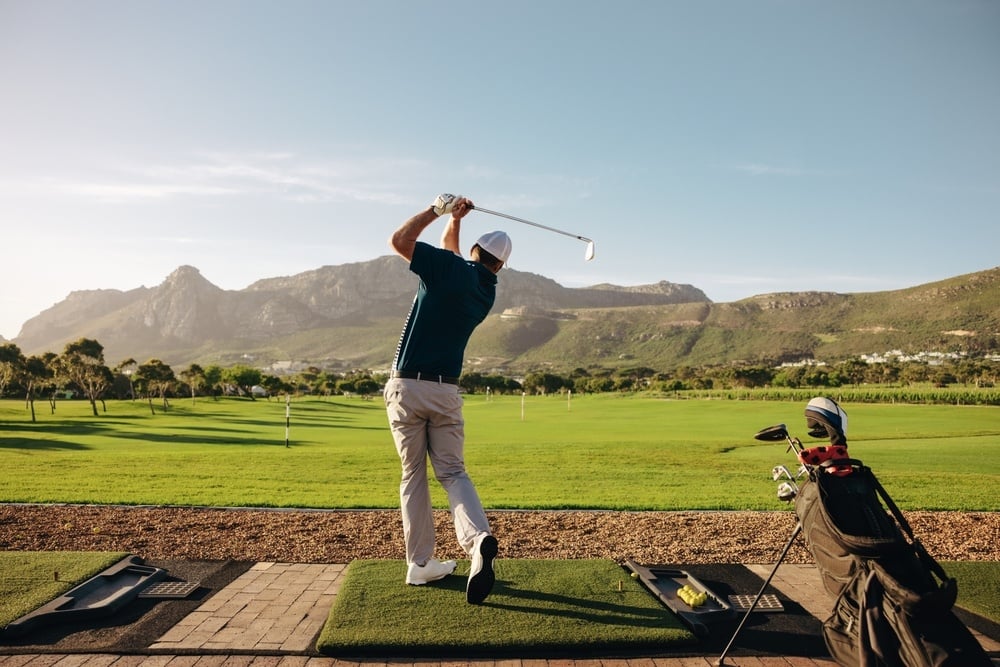 man playing golf, swinging at the ball on a sunny day